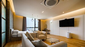 Een moderne woonkamer met een bank, fauteuils, een glazen salontafel en een flatscreen televisie aan de muur.