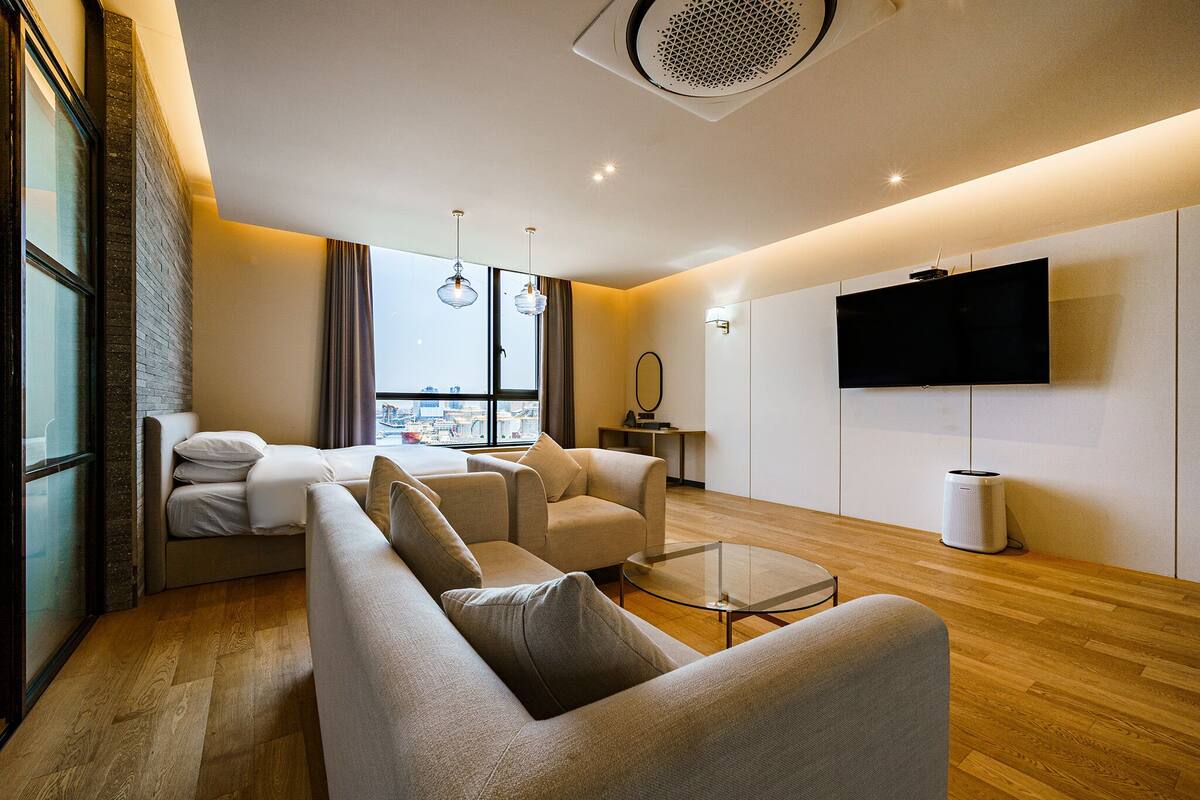 Ein modernes Wohnzimmer mit einer Couch, Sesseln, einem Glastisch und einem flachbildfernseher an der Wand.