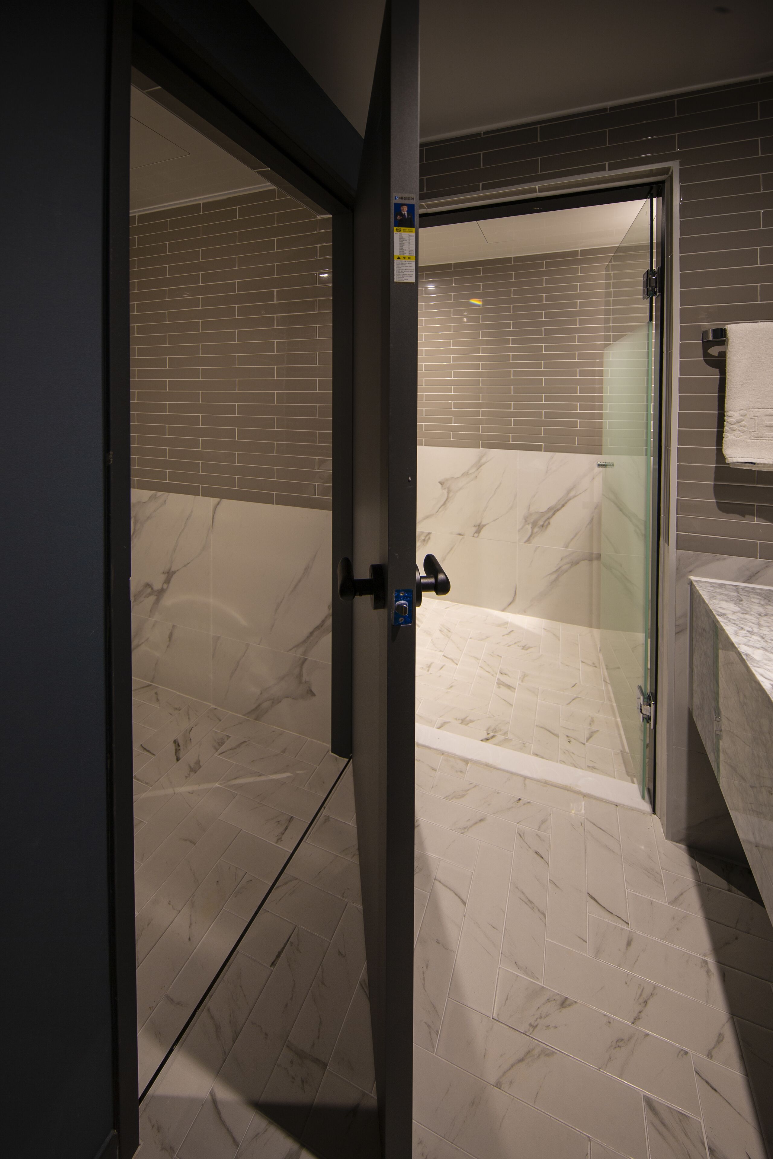 A modern bathroom with a glass shower door, a marble-tiled floor, and a brick wall.