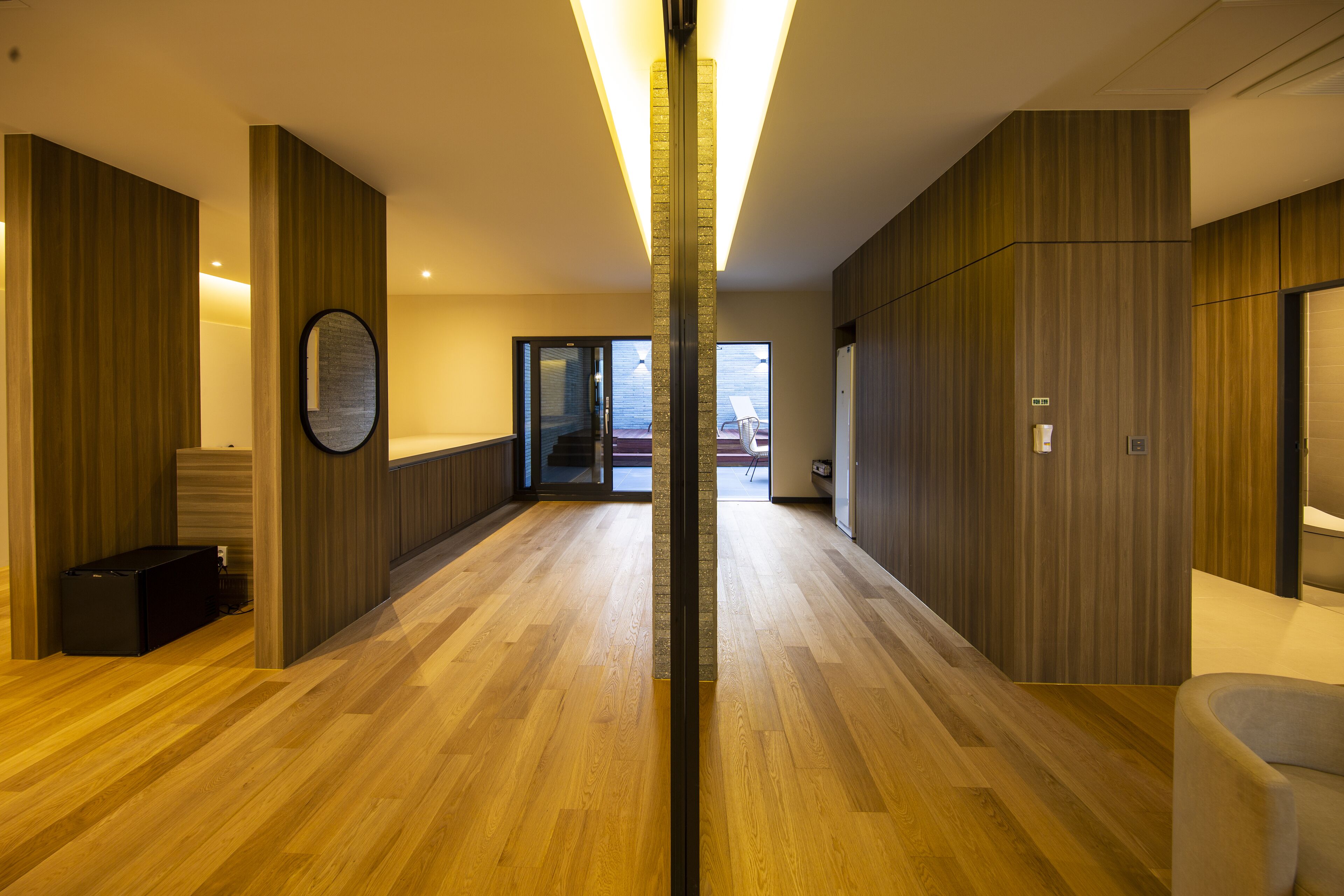 Un pasillo moderno de hotel con piso de madera, un accesorio de iluminación central y vistas al área exterior.