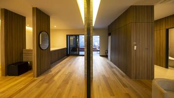 Un pasillo moderno de hotel con piso de madera, un accesorio de iluminación central y vistas al área exterior.