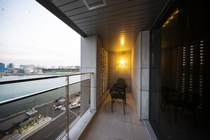 Un balcón con vistas al agua y al paisaje urbano, una mesa con sillas y una lámpara fijada a la pared.