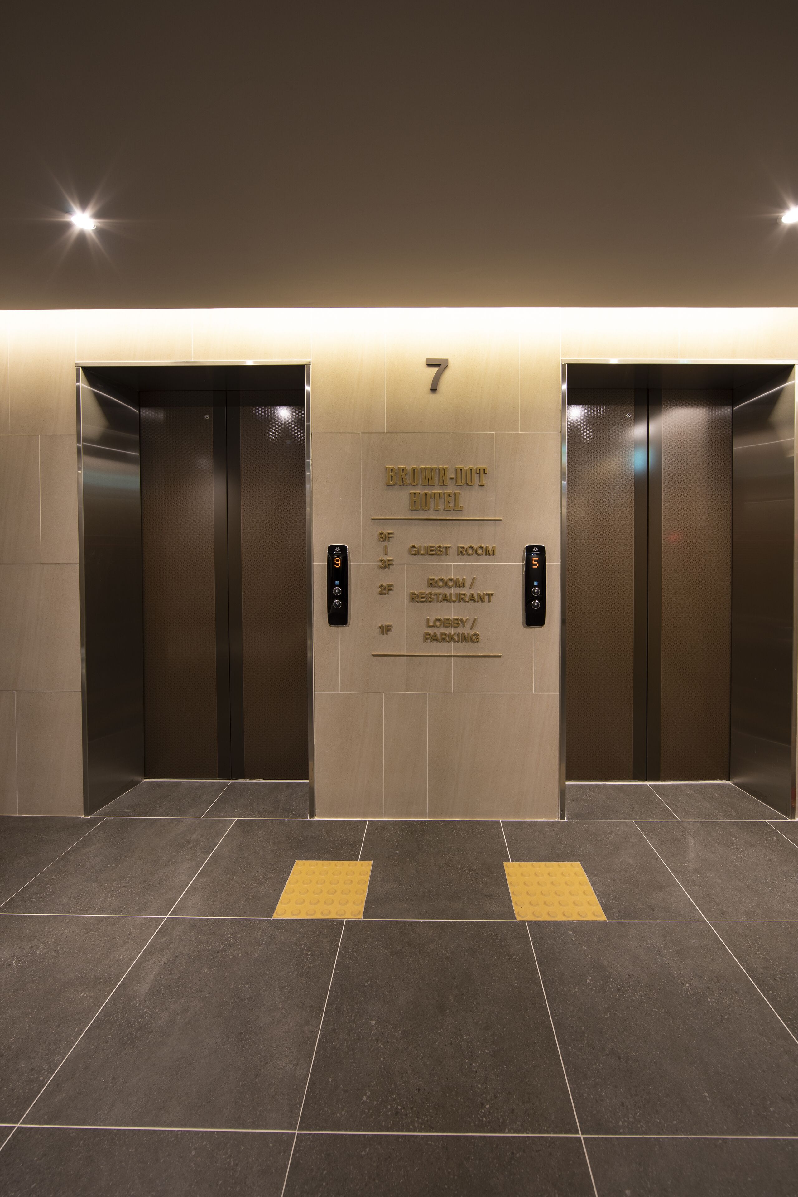 A modern elevator with a digital display indicating floor 7, and a sign above listing amenities including a guest room, restaurant, lobby, and parking.