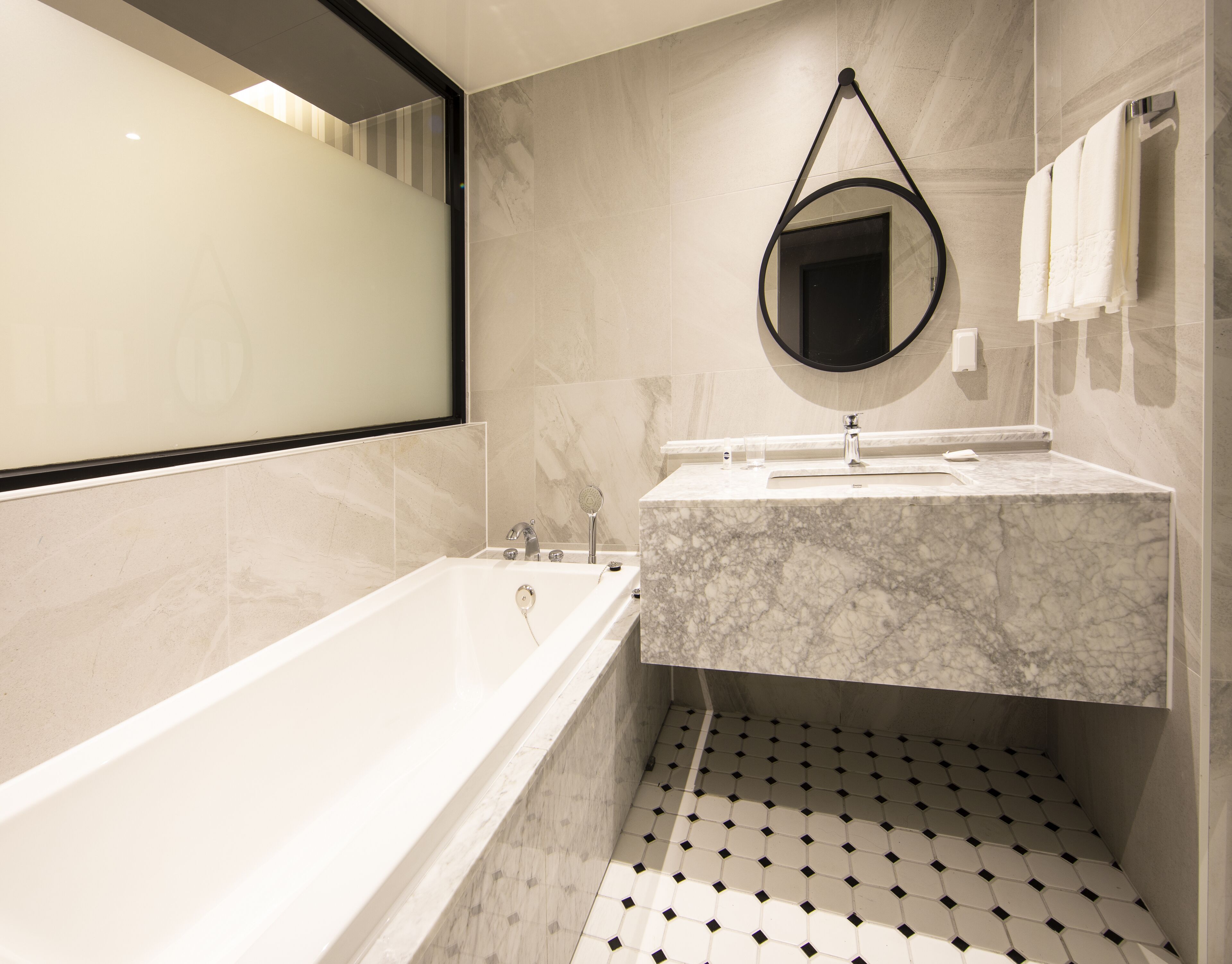 Un baño moderno con una bañera independiente, un lavamanos de mármol y un espejo grande.