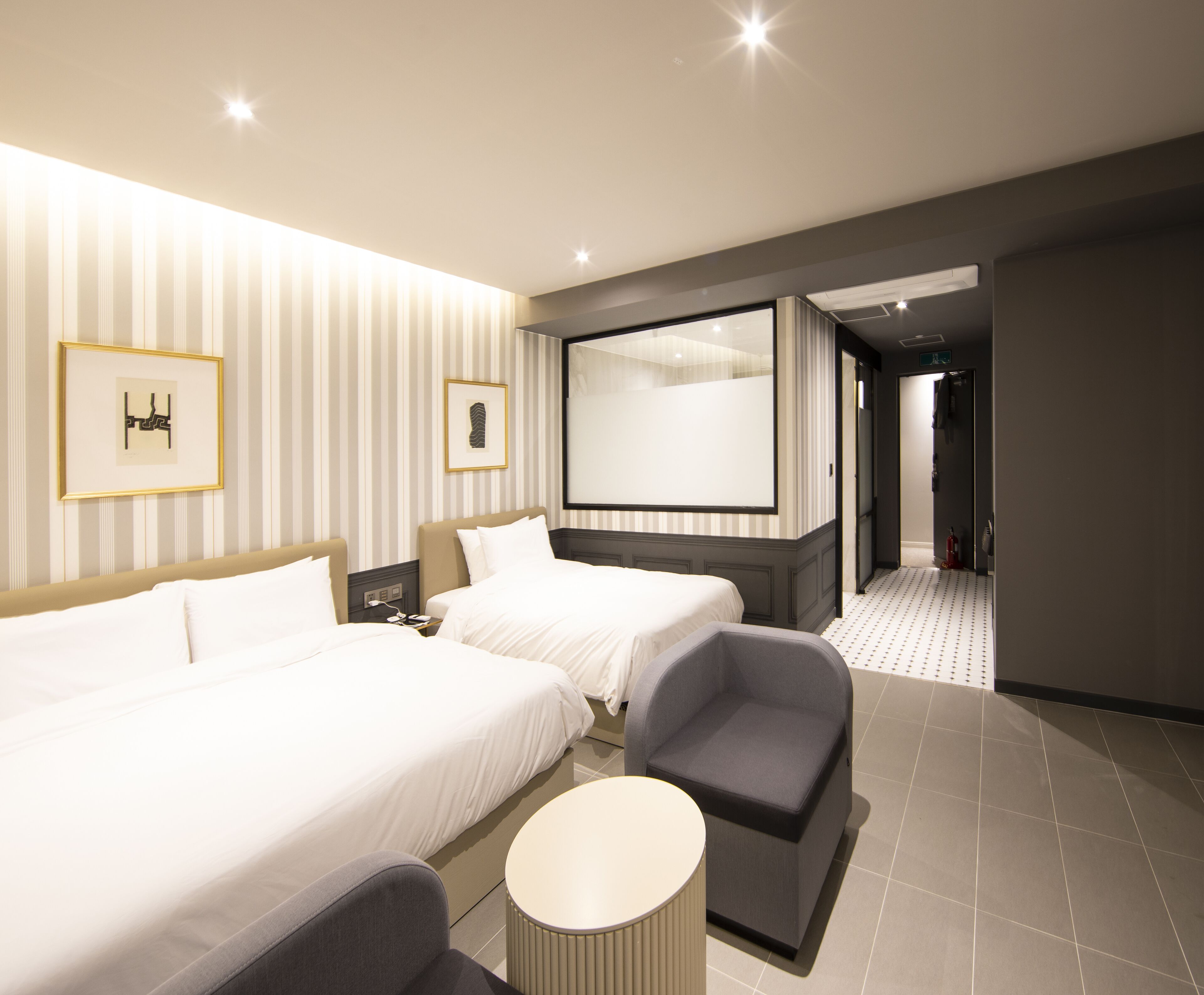 A hotel room with two beds, a seating area, a TV, and a bathroom visible through an open door.
