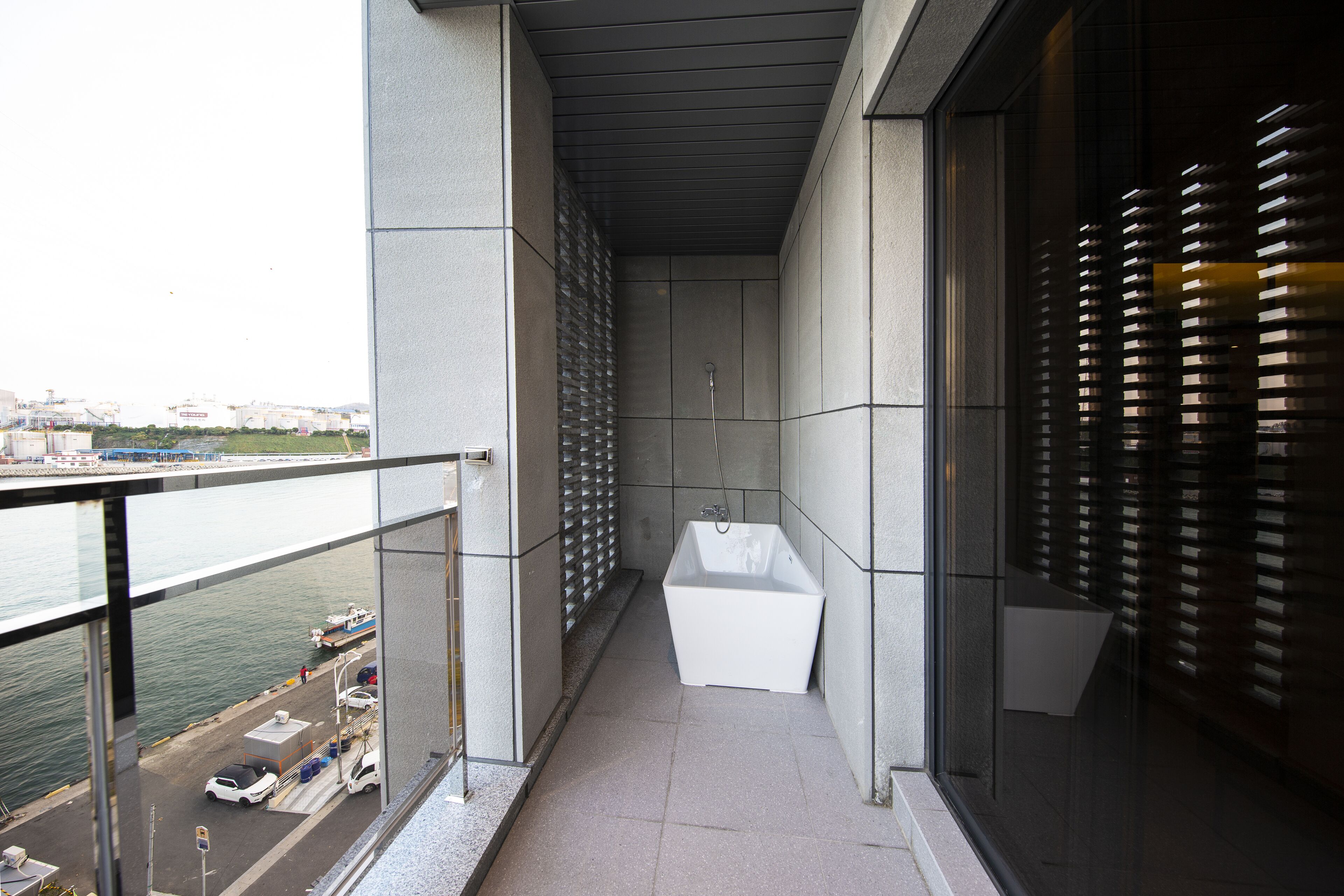 A narrow balcony with a view of the water and dock, a white bathtub, and a glass door with blinds.