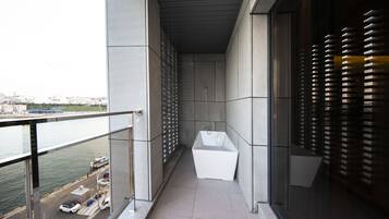 A narrow balcony with a view of the water and dock, a white bathtub, and a glass door with blinds.