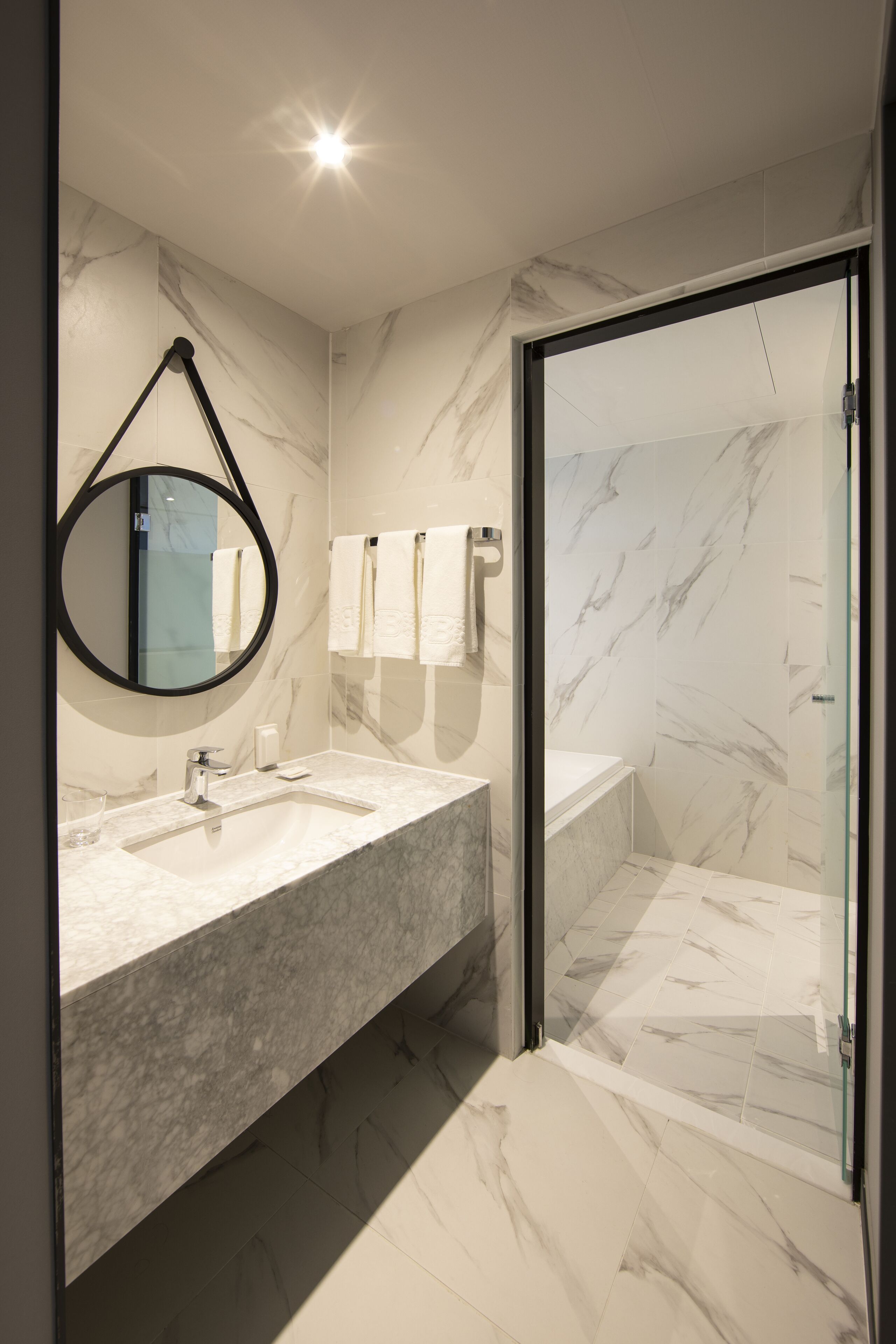Un baño moderno con tocador de mármol, cabina de ducha con mampara de vidrio y un espejo grande.