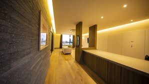 Een moderne hotellobby met een houten receptiebalie, een zithoek met een bank, en een uitzicht op de stadsplattegrond door grote ramen.
