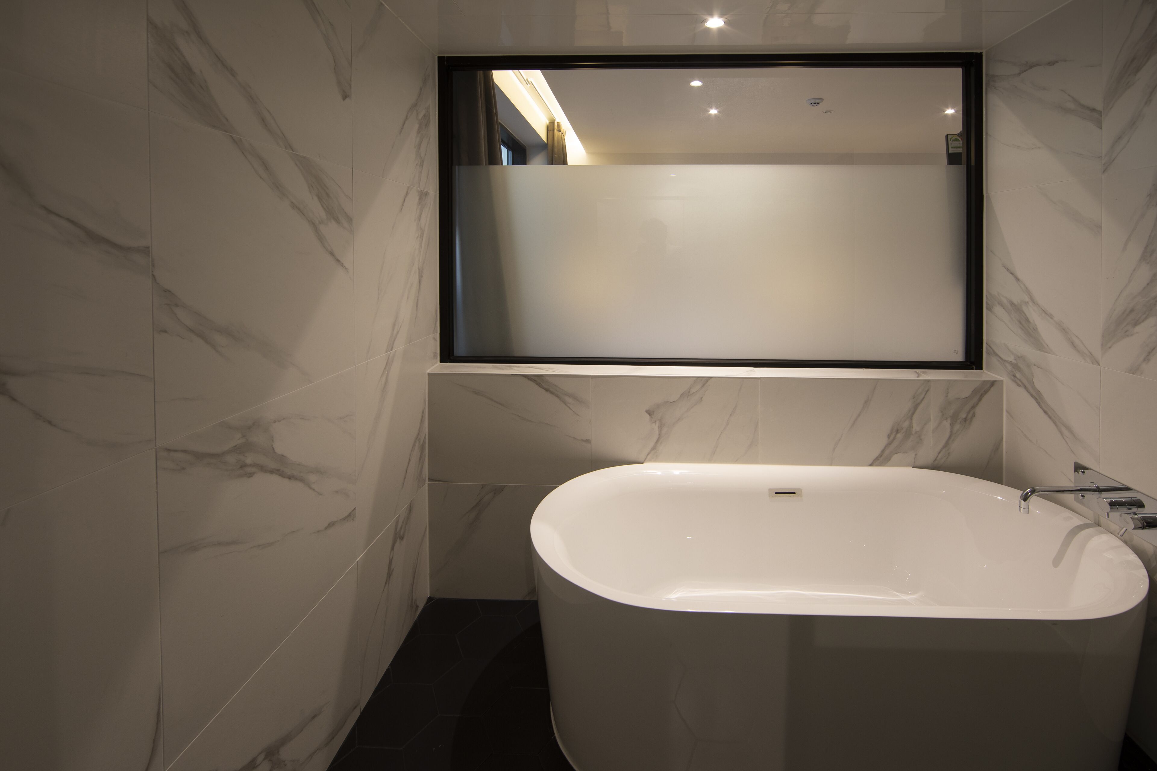 Un baño moderno con una bañera independiente, paredes de mármol y un espejo grande sobre la bañera.