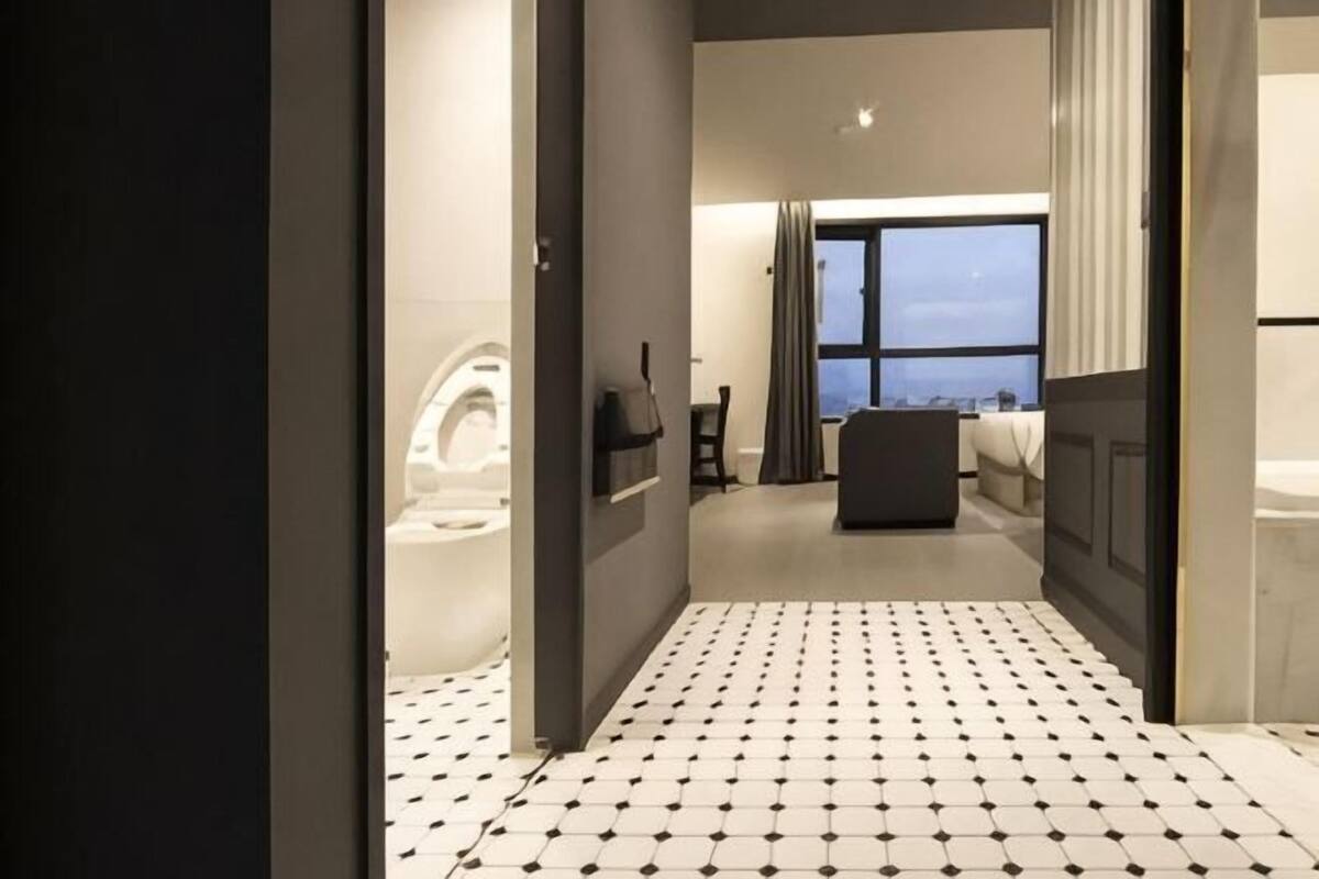 Ein Hotelzimmer mit Fliesenboden, einem Bett, einem Fenster und einem Badezimmer inklusive Toilette.