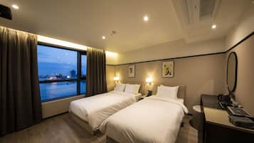 A hotel room with two beds, a large window with curtains, a desk with a telephone, and a coffee maker.