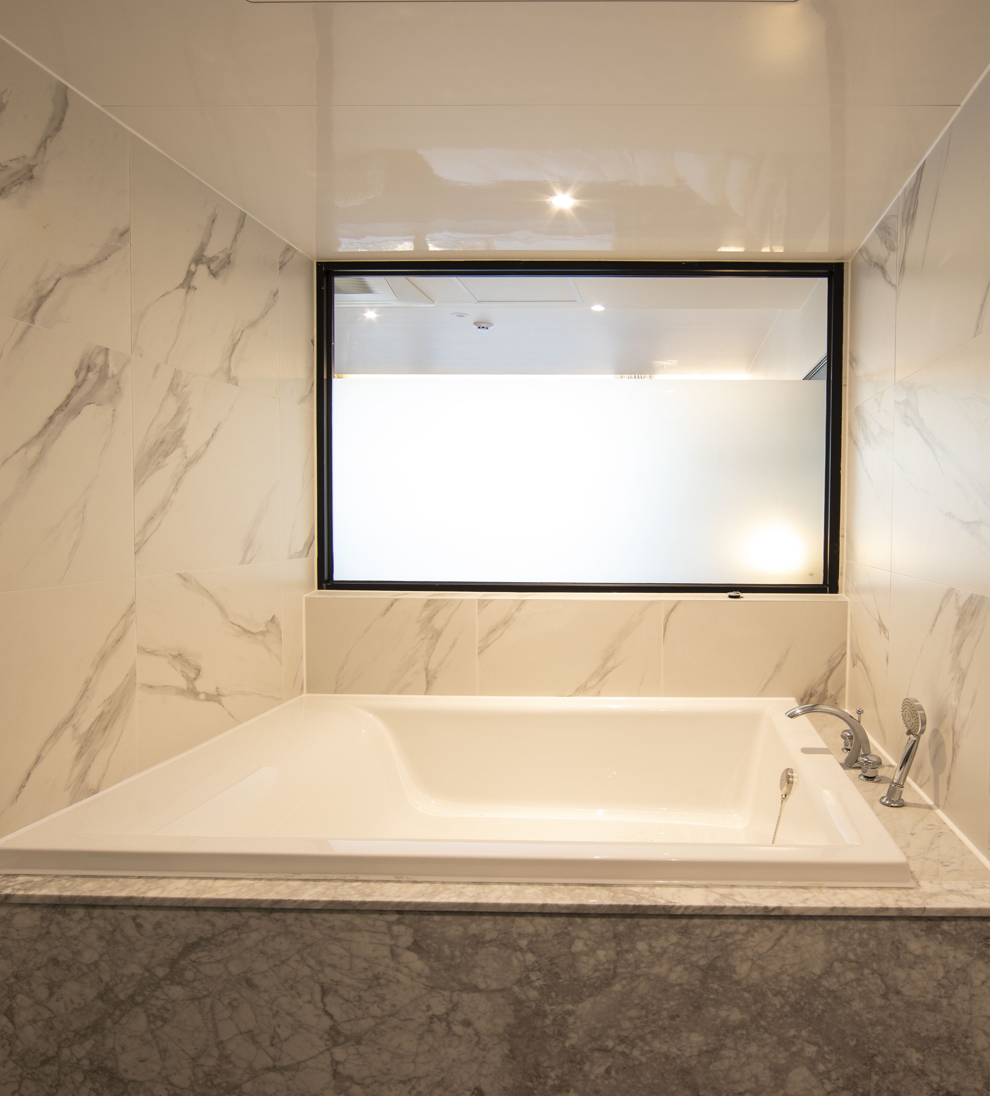 Ein modernes Badezimmer mit einer freistehenden Badewanne, Marmorwänden und einem großen Spiegel über der Wanne.
