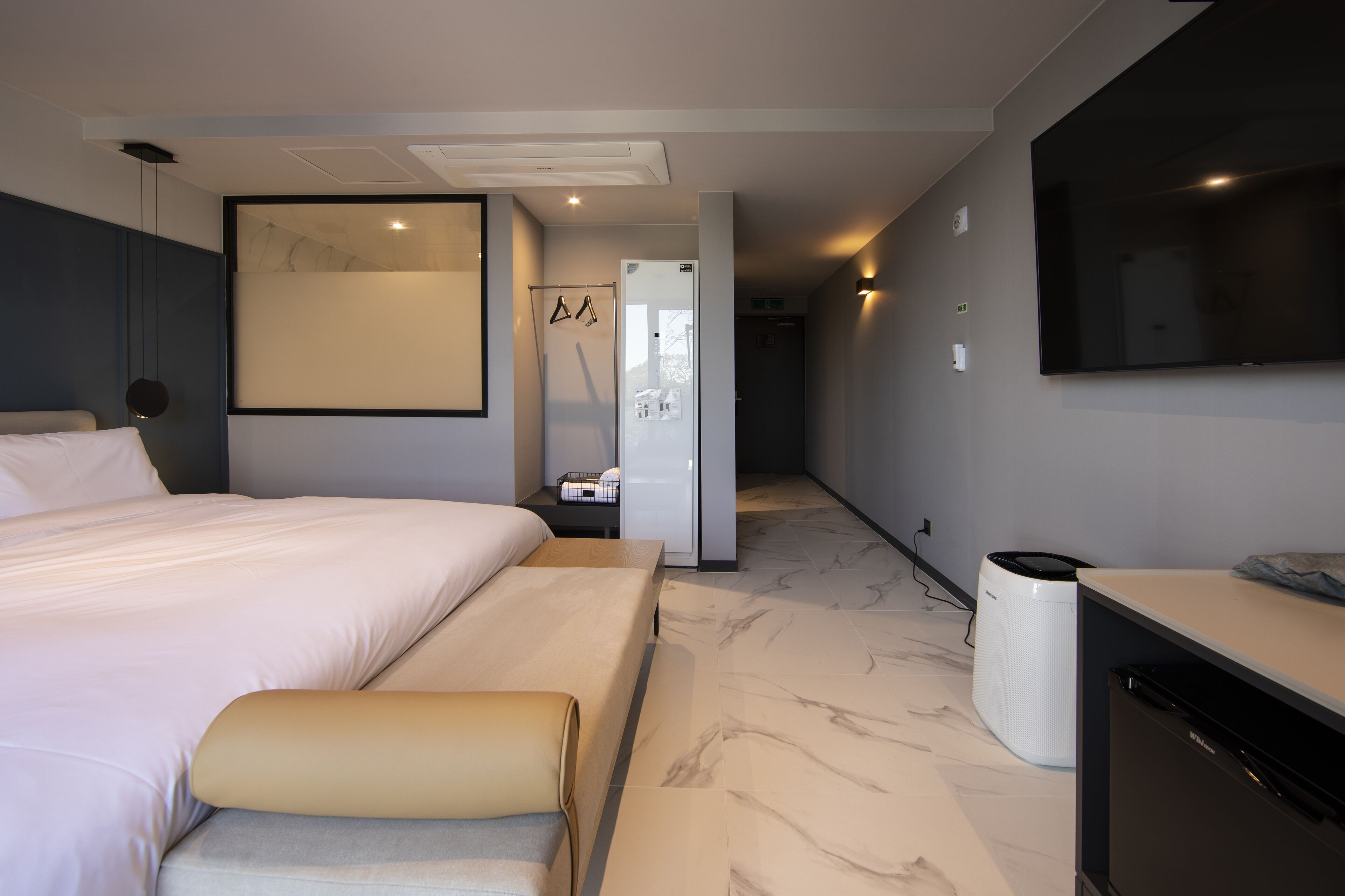 A modern hotel room with a large bed, a flat-screen TV, a built-in washing machine, and a bathroom with a shower and toilet.