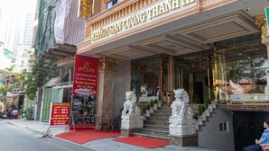 L’entrée d’un hôtel, avec une architecture richement décorée, un tapis rouge et une enseigne indiquant le nom de l’hôtel et la date de sa grande ouverture.