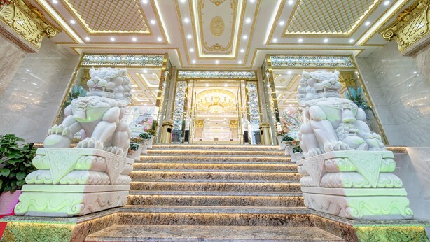 Un magnifique escalier orné de sculptures complexes menant à une vaste pièce somptueuse, illuminée par un lustre.