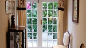 Un couloir avec un tapis à motifs, deux chaises, une petite table et un meuble contenant des objets décoratifs.
