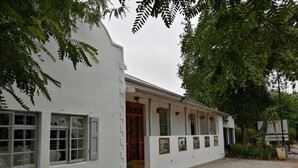 Un bâtiment blanc doté de nombreuses fenêtres et d’une porte, entouré de gravier et de verdure.