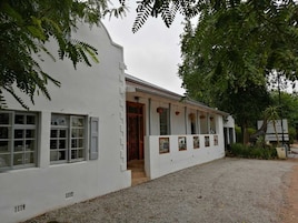 Um edifício branco com várias janelas e uma porta, rodeado por cascalho e vegetação.