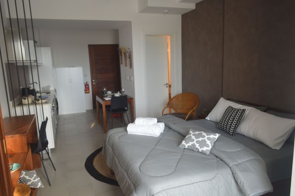 A modern hotel room with a large bed, a dining area, and a separate workspace.