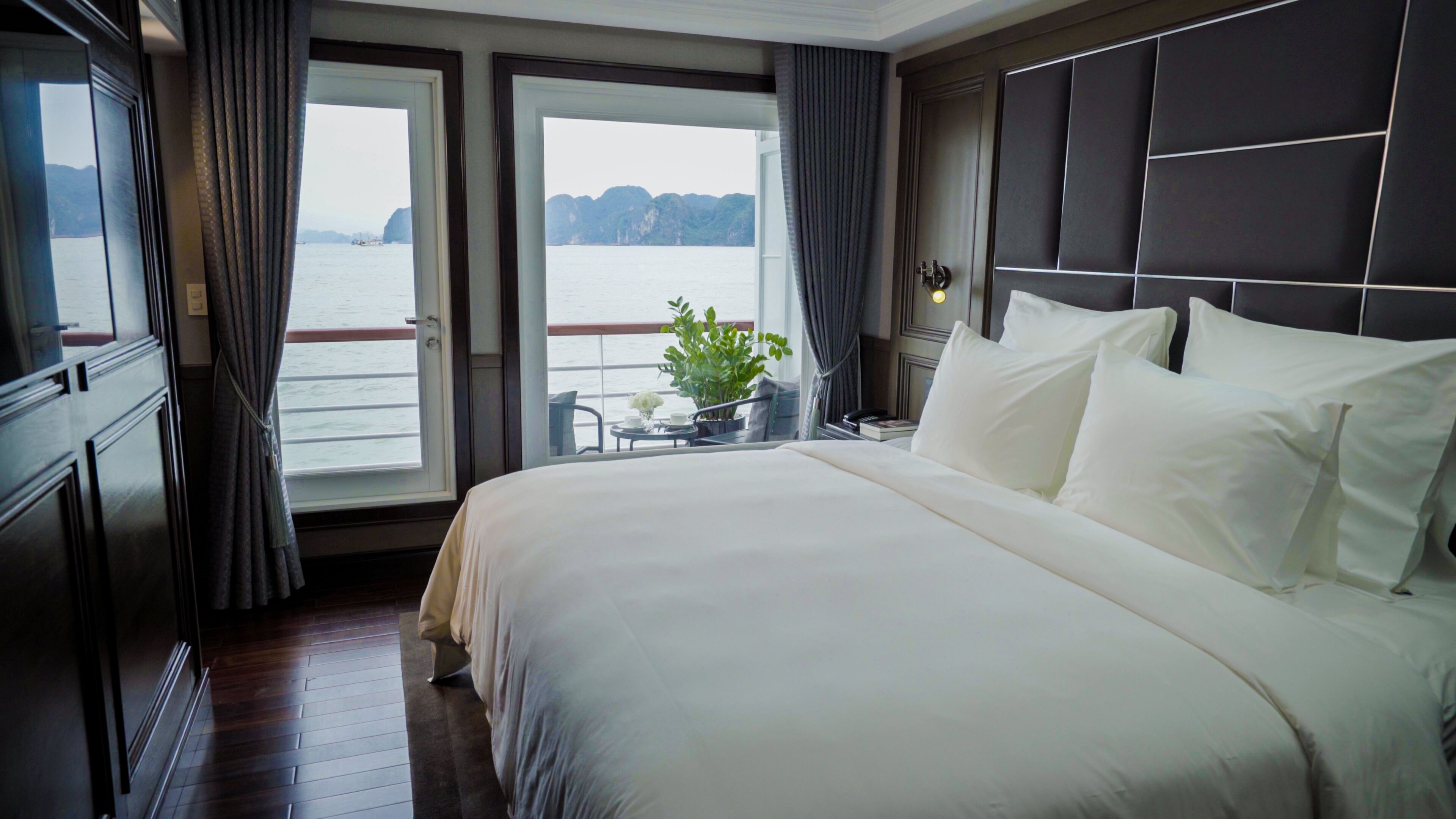 A hotel room with a large bed, a view of the water, and a balcony with a plant.