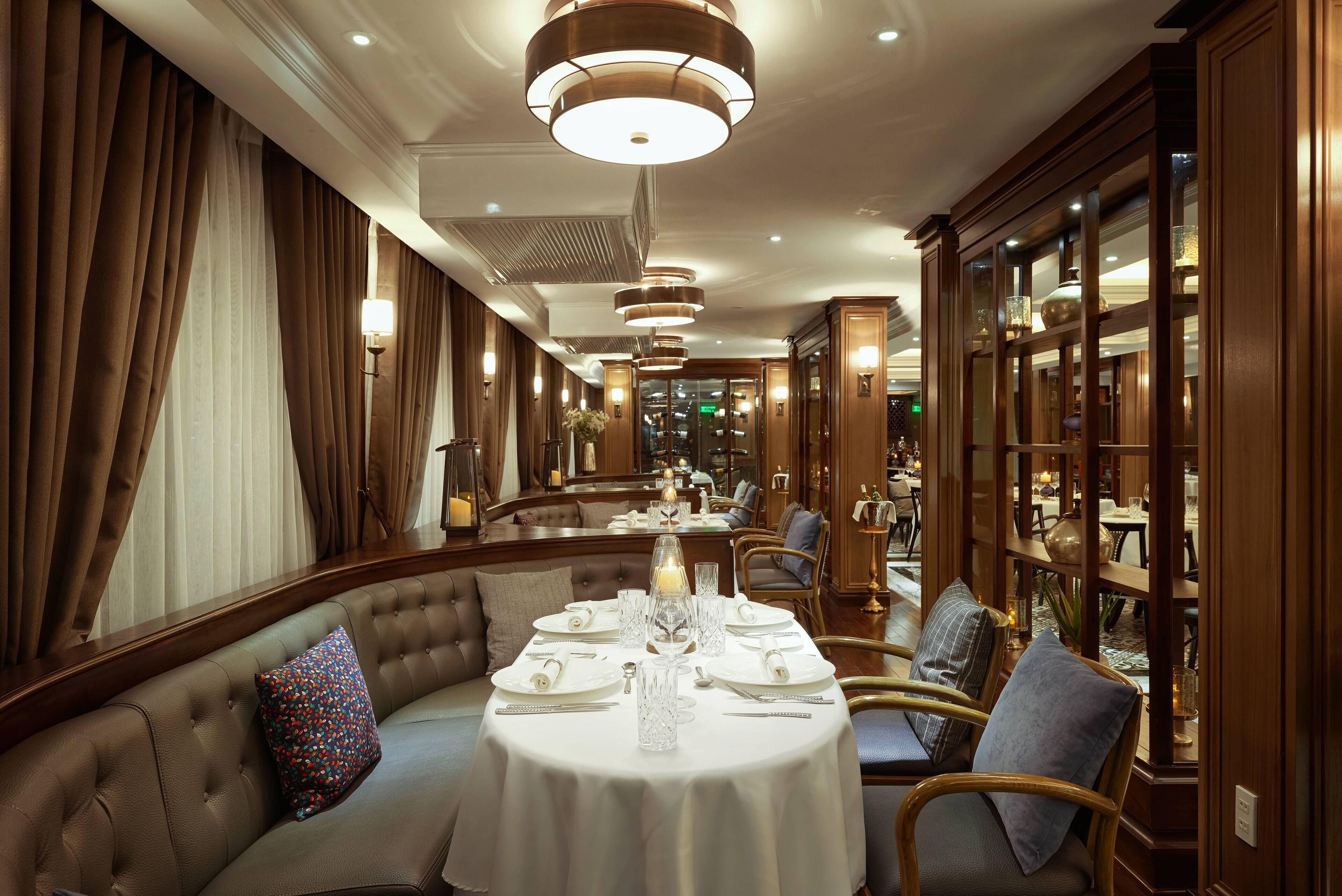 Un comedor formal con una mesa redonda preparada para cuatro personas, asientos tapizados y vista al interior del restaurante.
