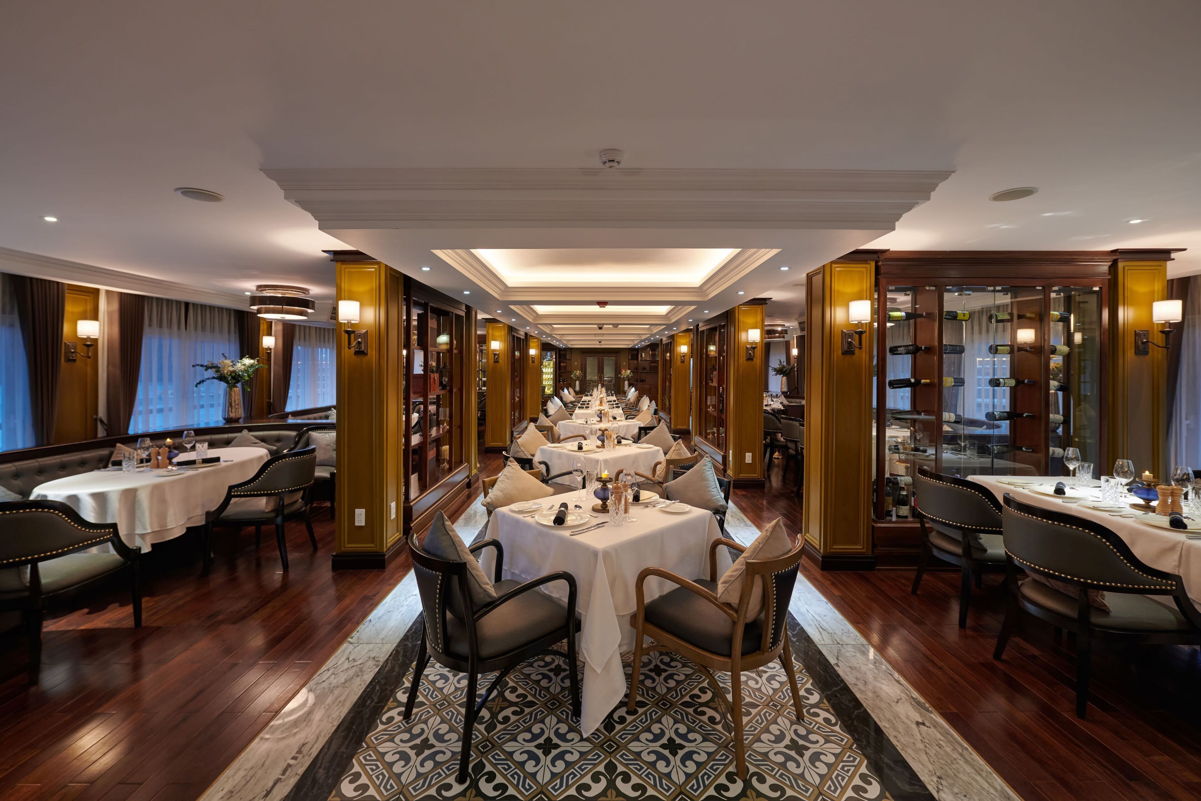 A formal dining room with multiple tables and chairs, elegant lighting, and a patterned carpet.