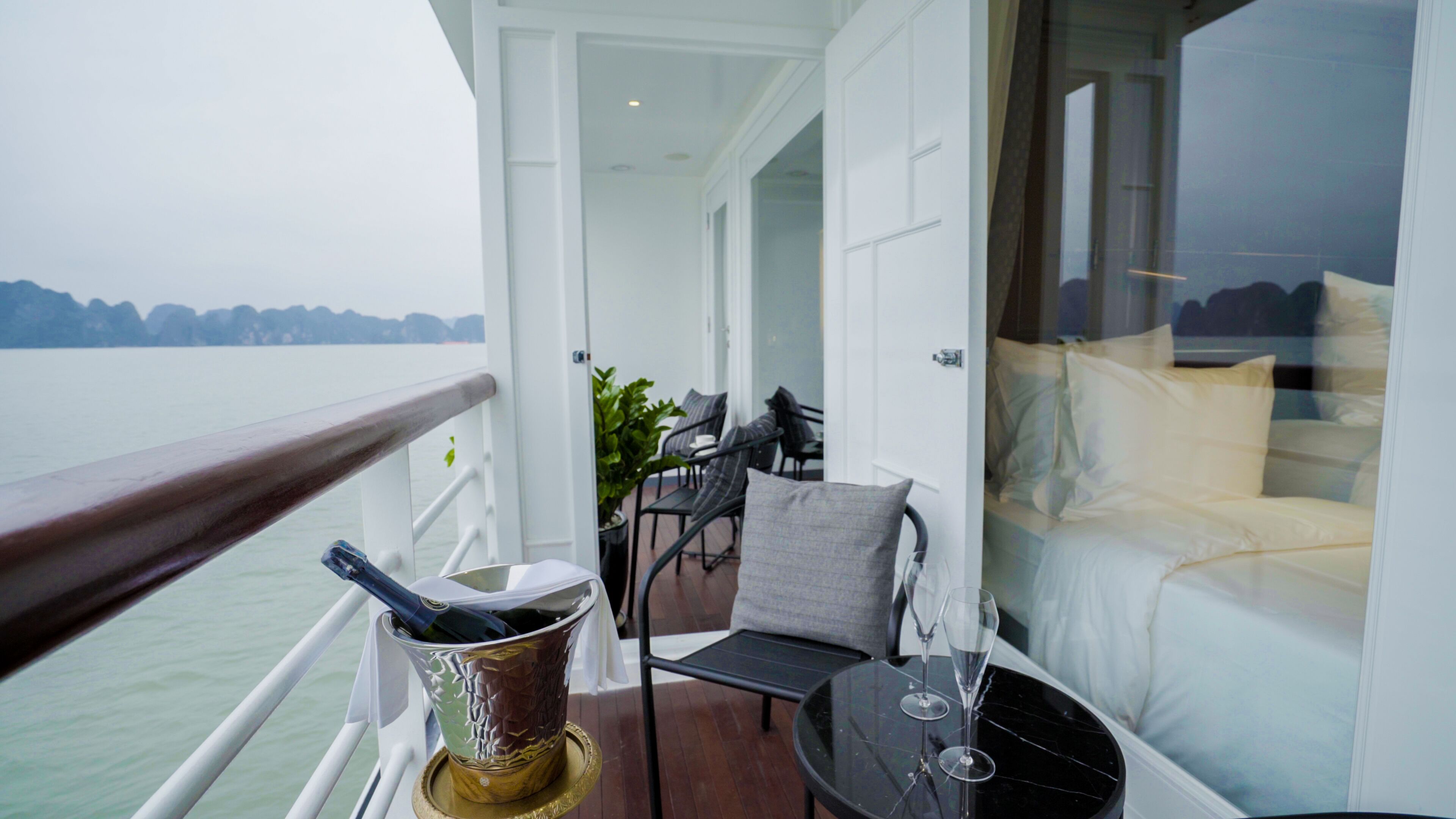 Un balcon avec vue sur l’eau, une table avec une bouteille et des verres, et un canapé avec des coussins.