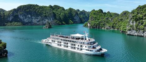 A large, multi-deck river cruise ship with "Paradise Grand" written on the side, navigating through a turquoise river surrounded by lush green cliffs.