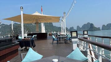 A deck with outdoor seating, a covered area, and a view of the sea and mountains.