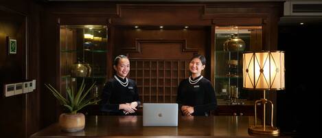 A reception desk with two staff members, a laptop, and a lamp.