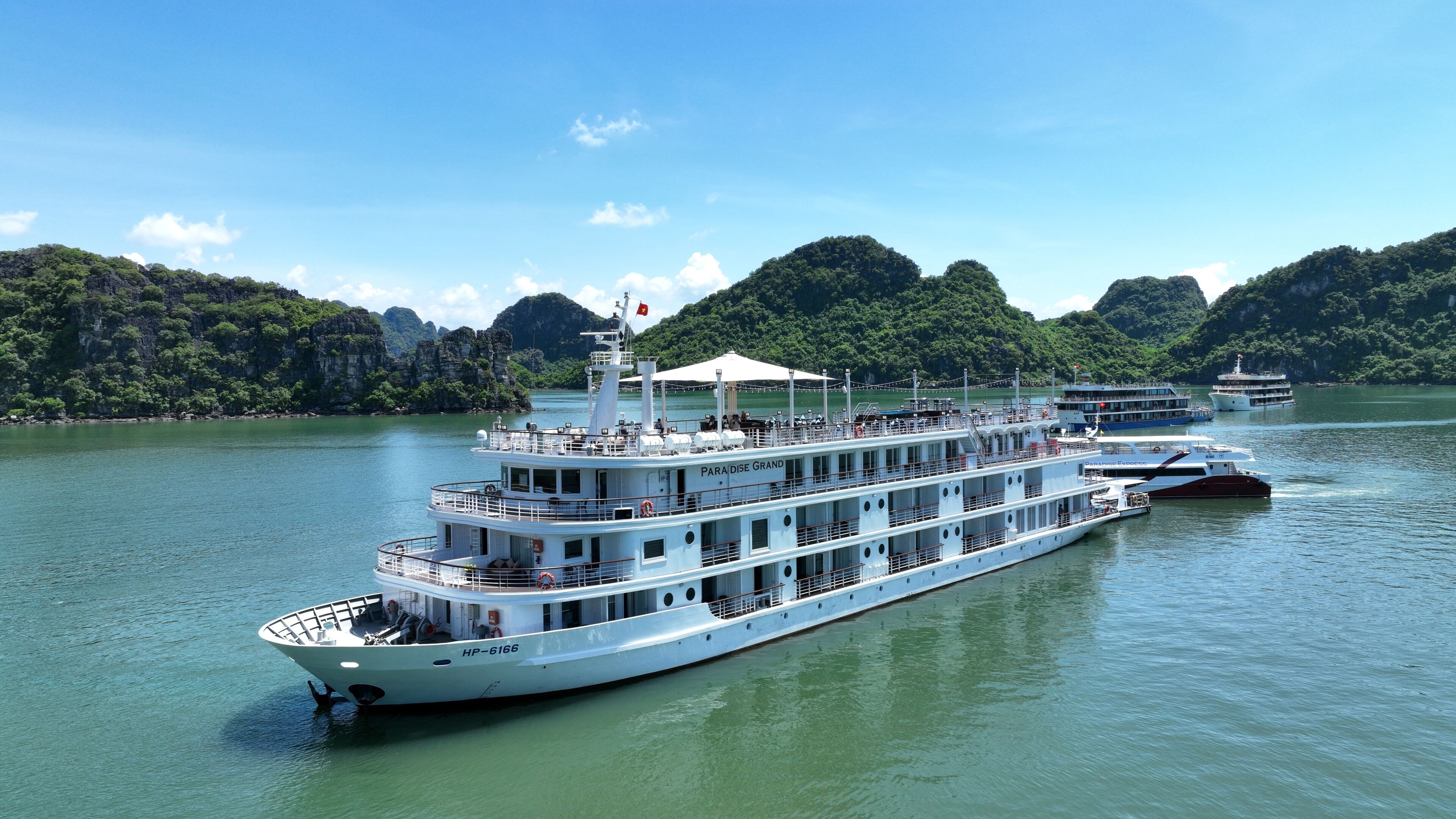 Un grand navire de croisière fluviale, doté de plusieurs ponts et d’une coque blanche, est amarré dans une rivière paisible, entourée de collines verdoyantes.