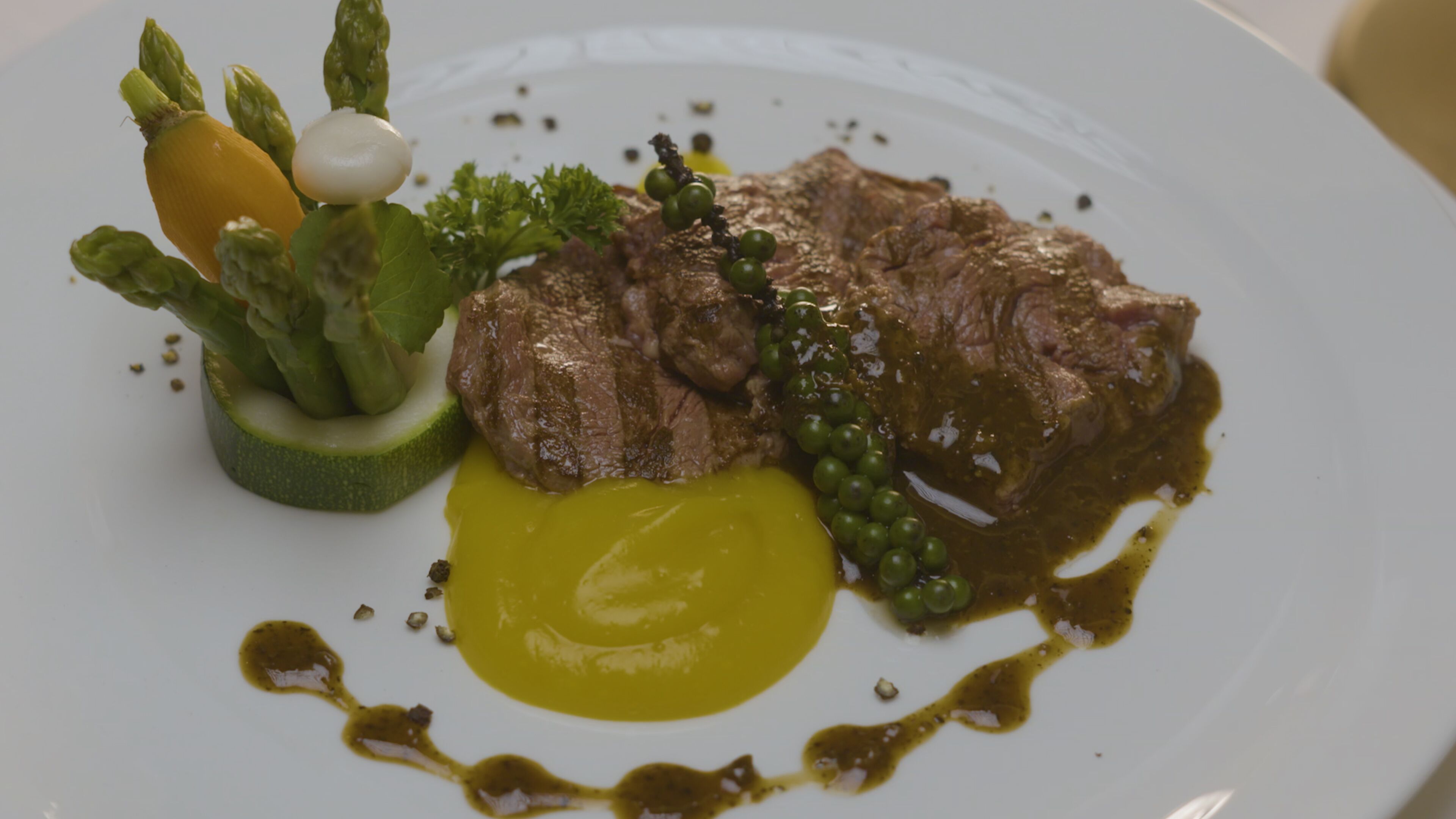 Ein Teller mit einem Steak, Spargel, Erbsen und einer Soßenportion.