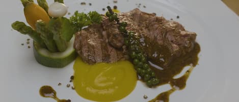 Ein Teller mit einem Steak, Spargel, Erbsen und einer Soßenportion.