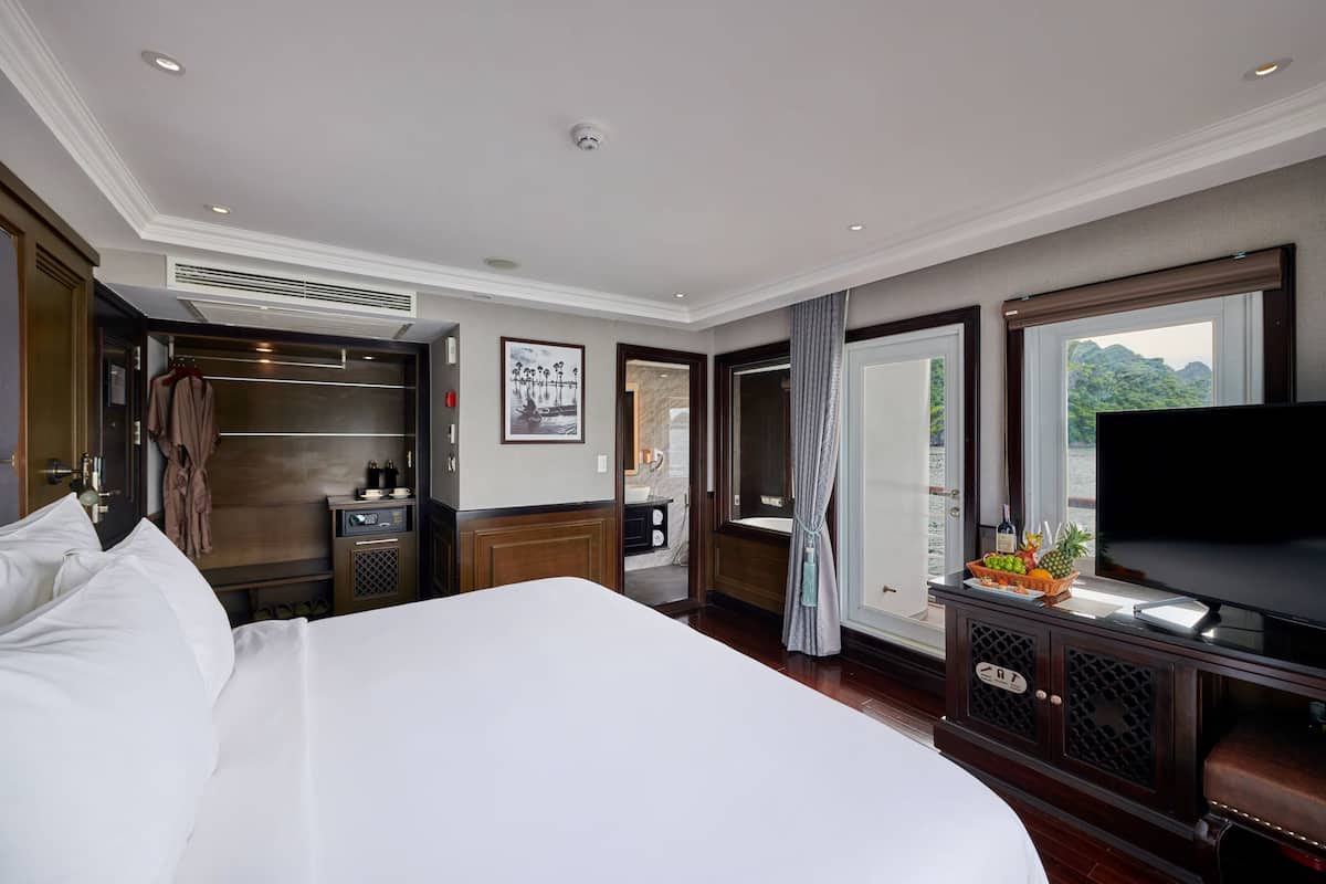 Ein Hotelzimmer mit einem großen Bett, einem Fernseher, einer Minibar und Blick ins Freie.