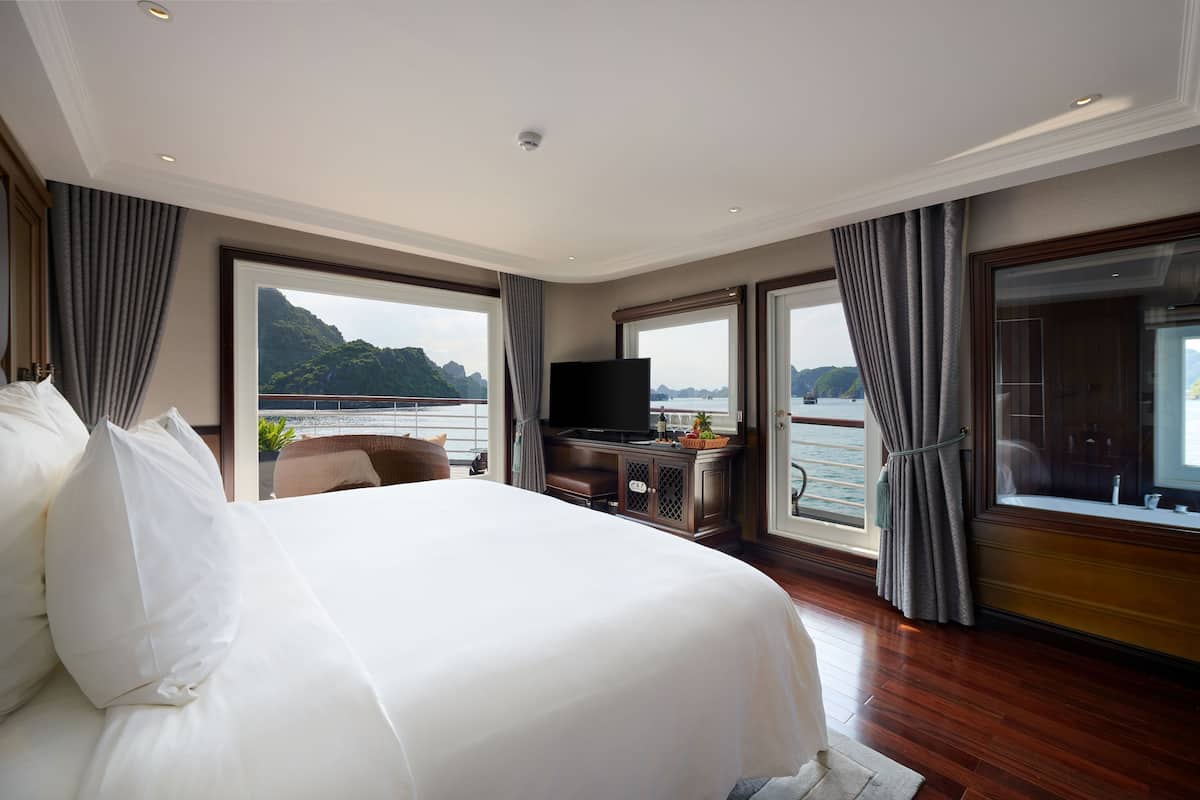 Ein Hotelzimmer mit einem großen Bett, einem Fernseher und Blick auf das Meer.