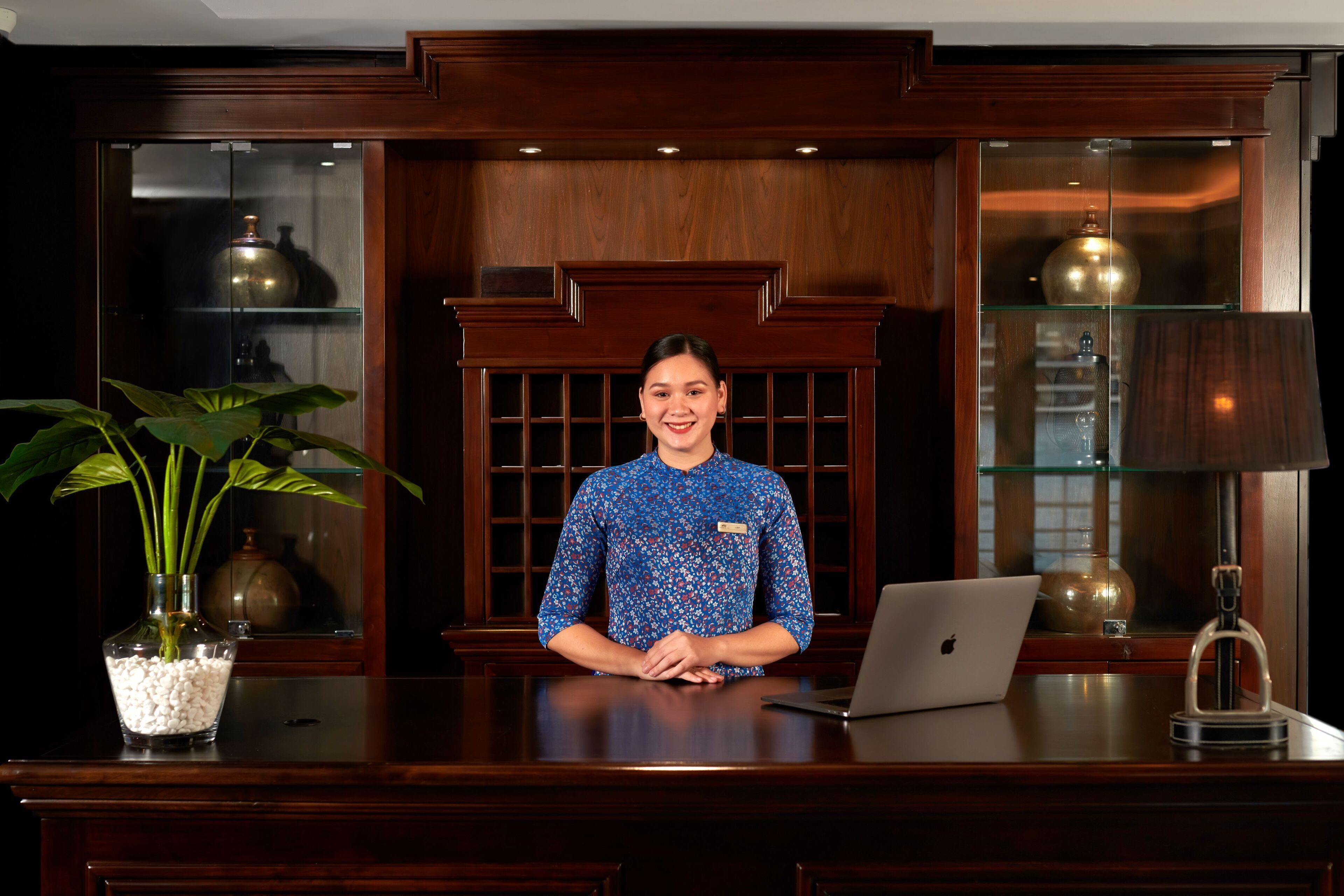 A reception desk with a laptop, a vase with white pebbles, and a potted plant.
