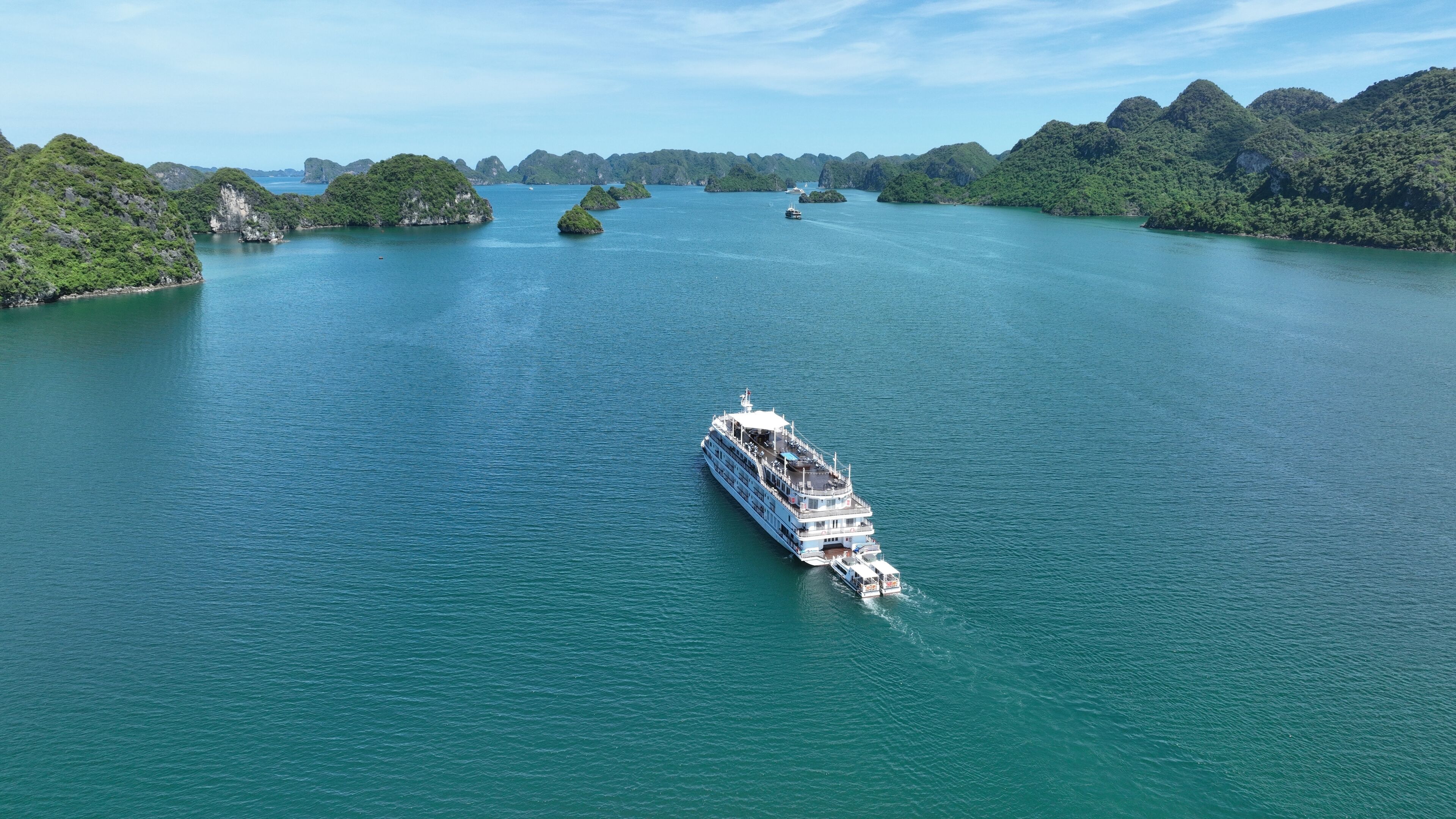 Un gran crucero navegando sobre un mar turquesa y tranquilo, rodeado de islas verdes y exuberantes.