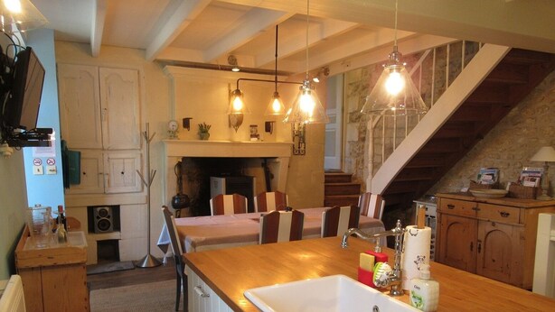 A cozy kitchen with a wooden countertop, white cabinets, and a built-in stove. There are hanging pendant lights, a fireplace, and a staircase leading to an upper level. - 4 - Star Holiday Home on the Charente River. (Bourg-Charente)
