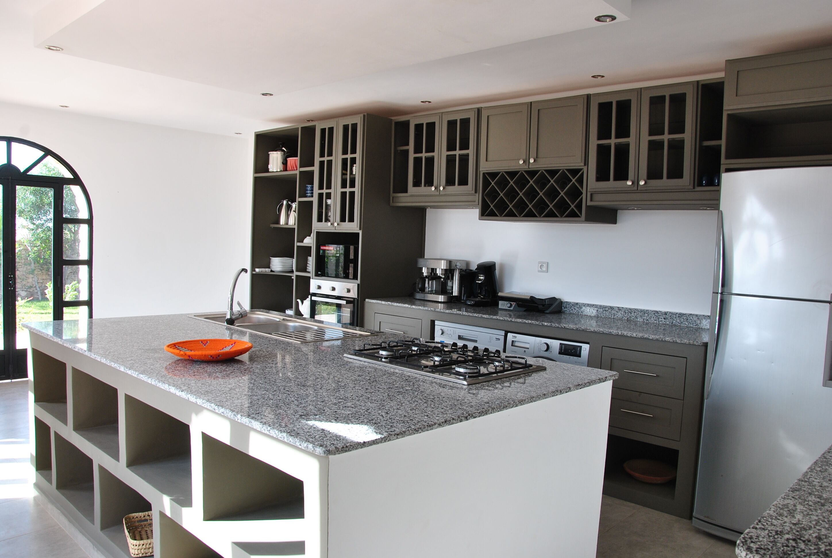 A modern kitchen with a central island, built-in cabinets, and a stainless steel refrigerator.