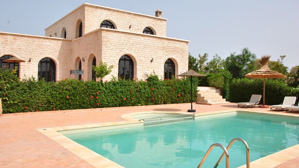 A pool area with a stone building, a clear sky, and a well-maintained garden. - Villa l "Ambre d'Essaouira (Essaouira)