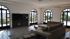 A modern living room with a sofa, a coffee table, and a TV. There are large windows with arched tops. - Villa l "Ambre d'Essaouira (Essaouira)