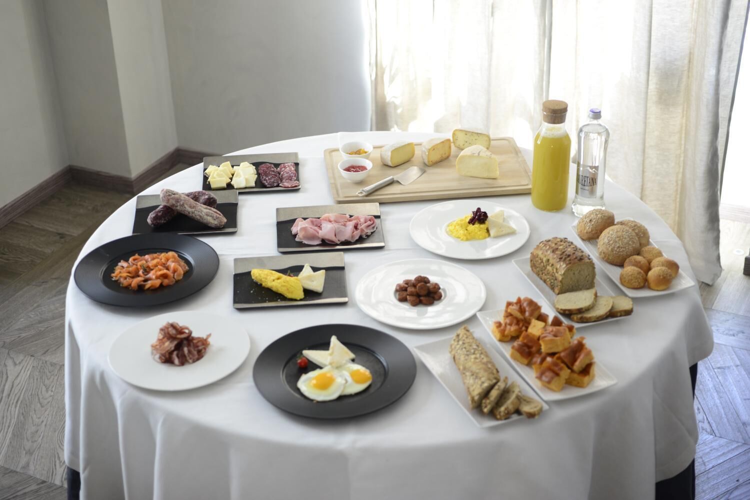 A breakfast buffet with various cheeses, cured meats, pastries, and eggs.