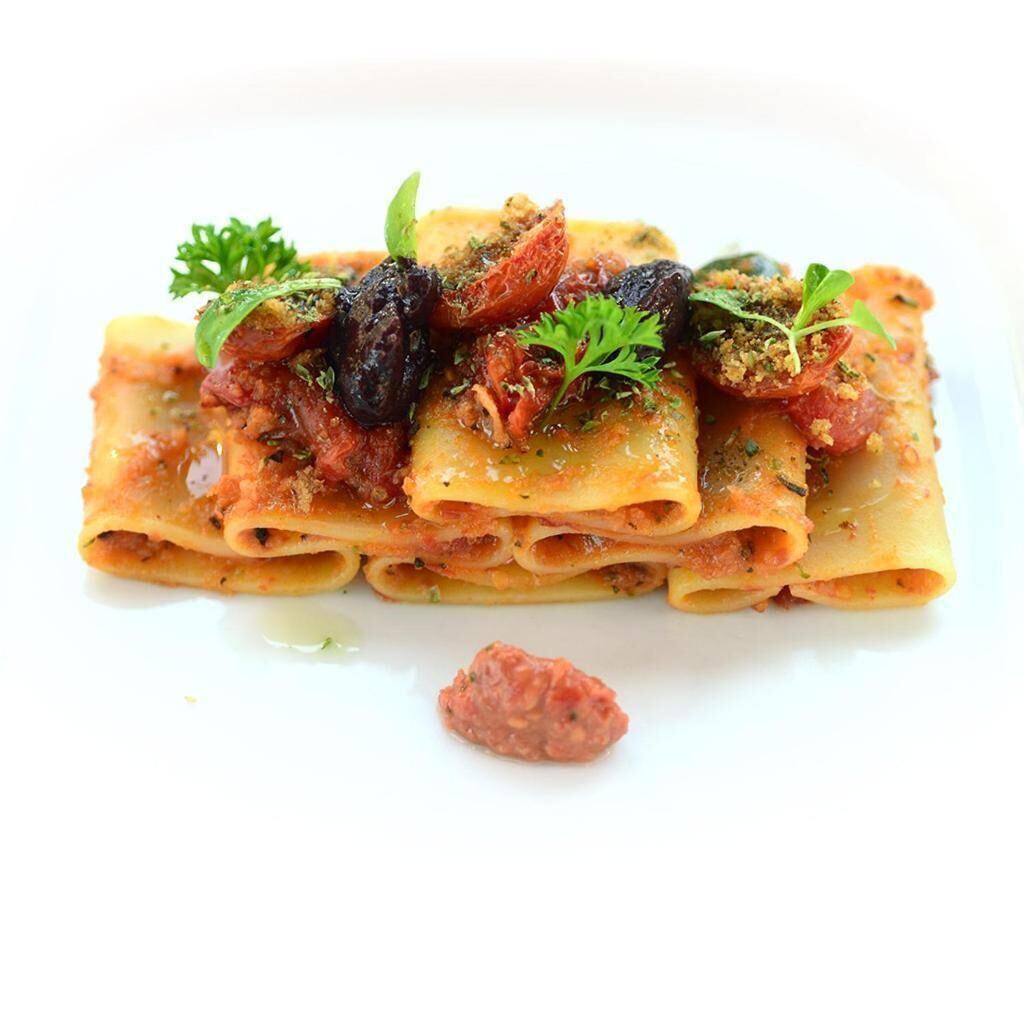 Een bord pasta met tomatensaus, gegarneerd met kruiden en mogelijk wat vlees.