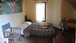 A bedroom with a zebra-patterned bedspread, a wooden chair, a small desk, and a painting on the wall.