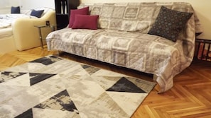 A living room with a patterned sofa, a geometric rug, and a wooden herringbone floor. - Studio Apartman Vijenac (Osijek)