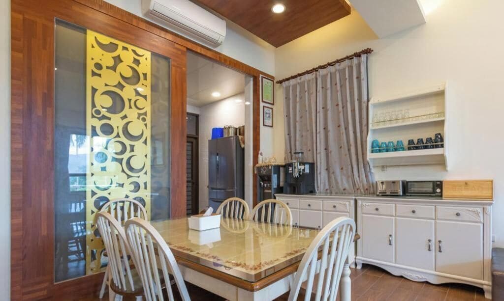 Un comedor con una mesa de vidrio y sillas, un armario blanco con estantes y un panel decorativo con motivos circulares.