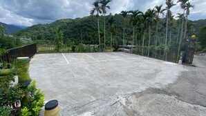 A tennis court surrounded by a fence, with palm trees and a hilly landscape in the background. - Atayal Villa (Datong)