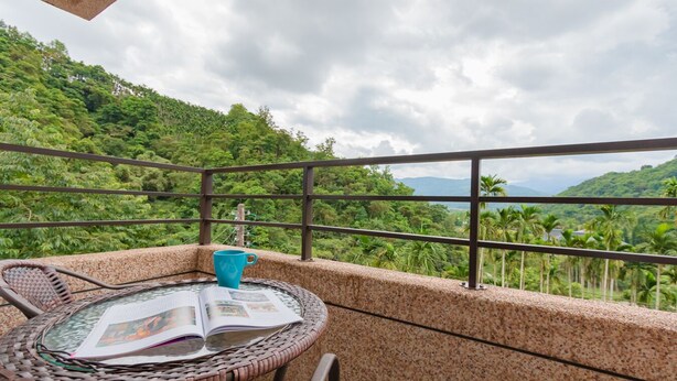 A balcony with a round table, a blue cup, and a magazine. The balcony overlooks a lush green landscape with palm trees and distant mountains. - Atayal Villa (Datong)