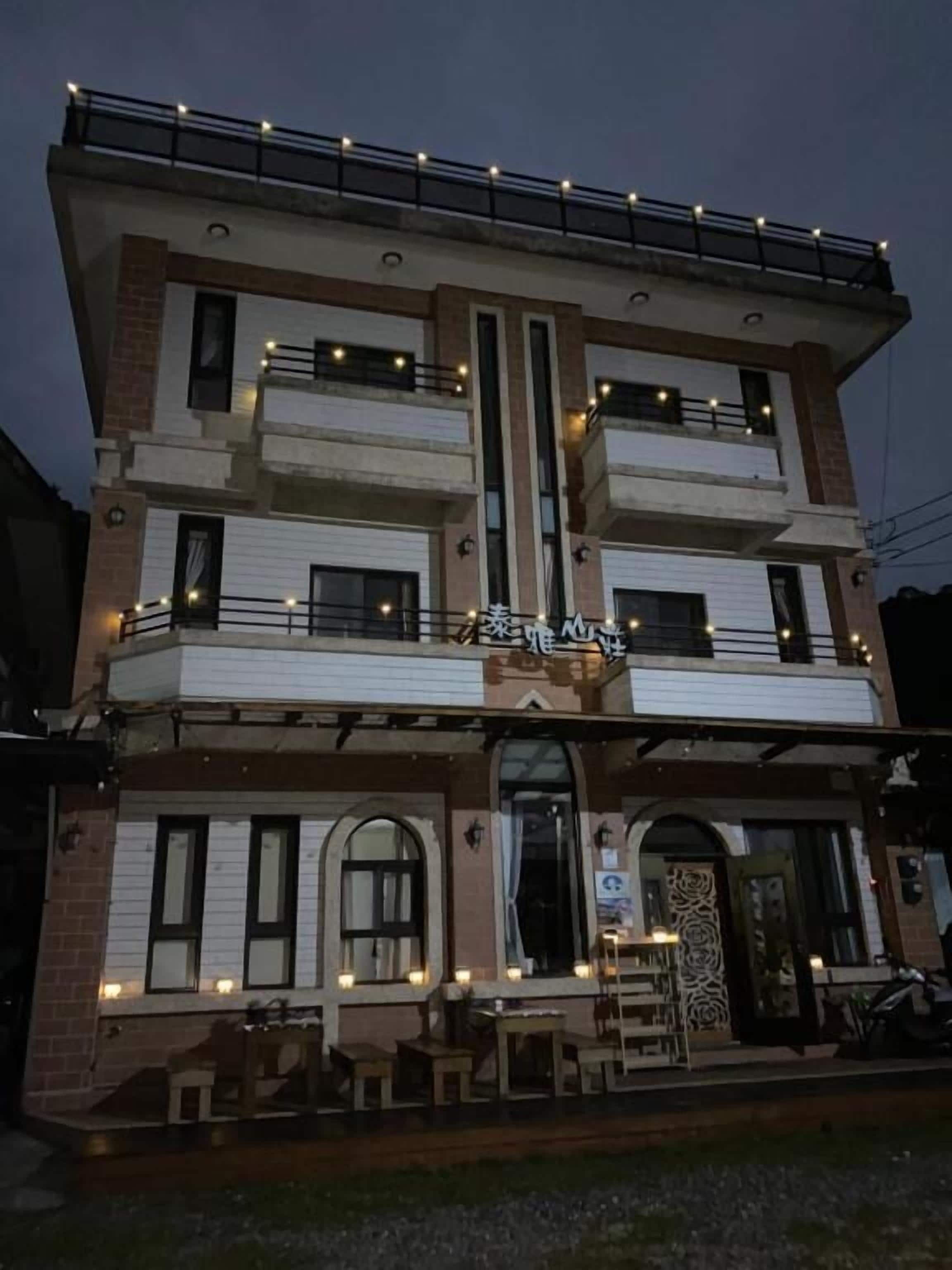 Un edificio de varios pisos con un balcón en el piso superior, una zona de estar al aire libre cubierta y un letrero con caracteres chinos.